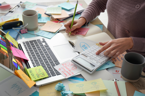 Woman working at a busy desk with laptop and notes, balancing work while retraining as a life coach