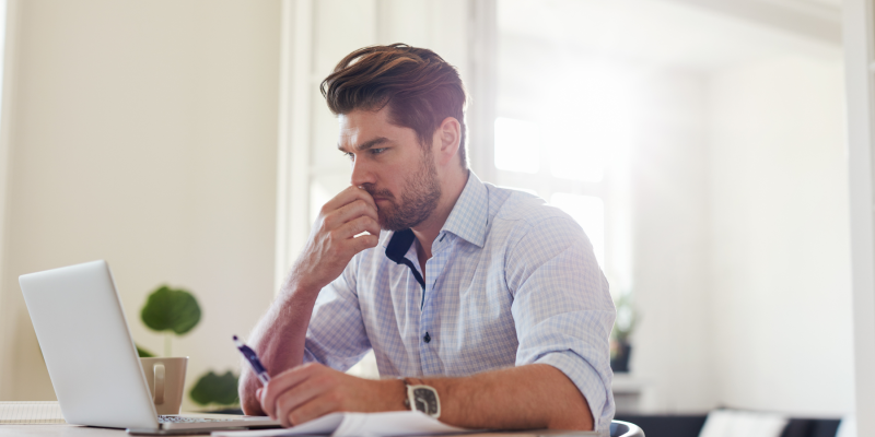Man considering the cost of life coach training in the UK while working at his laptop