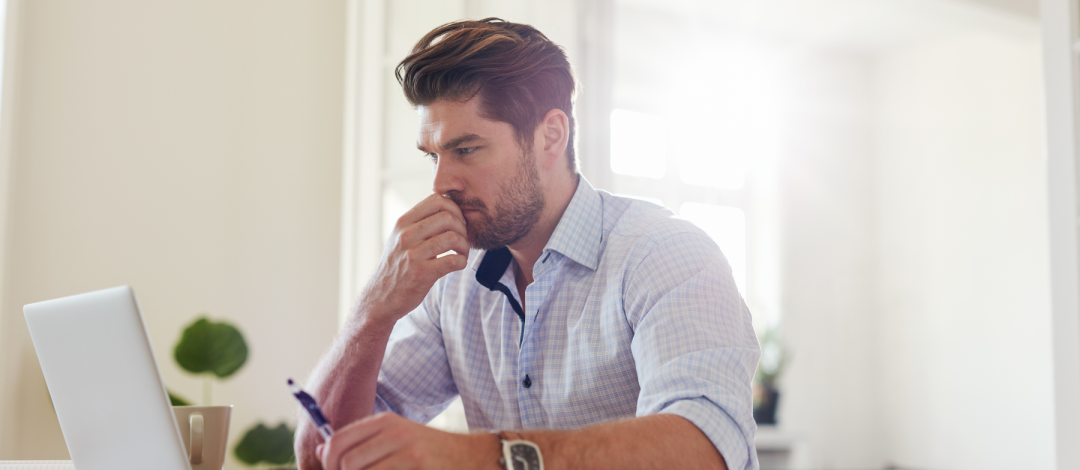 Man considering the cost of life coach training in the UK while working at his laptop